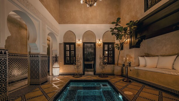 A luxurious indoor pool area with ornate tile work, a seating area with cushions, and a chandelier. - Riad Dar Yuba  (Marrakech)
