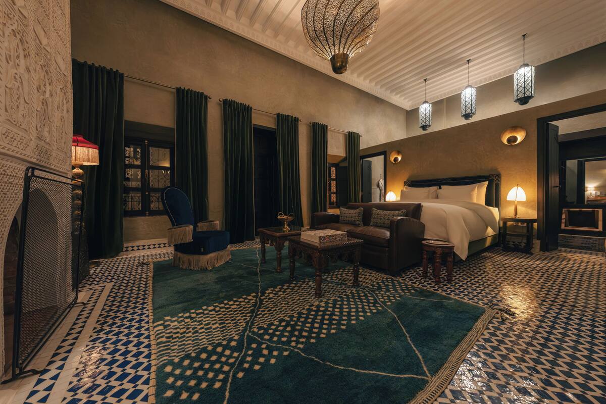 A hotel room with a patterned floor, a large bed, a sitting area with a chair and a small table, and a decorative ceiling light.
