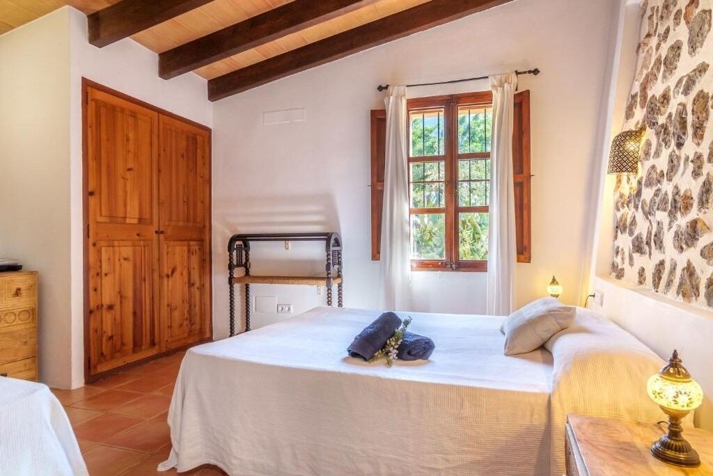 Une chambre à coucher avec un lit, une armoire en bois, une fenêtre avec des rideaux et un mur orné d’un motif.