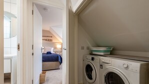 Un'area lavanderia con lavatrice e asciugatrice, un letto con coperta blu e un piccolo contenitore sopra l'asciugatrice.