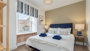 Una camera da letto con un letto, due comodini, una finestra con tende e vista sugli edifici.