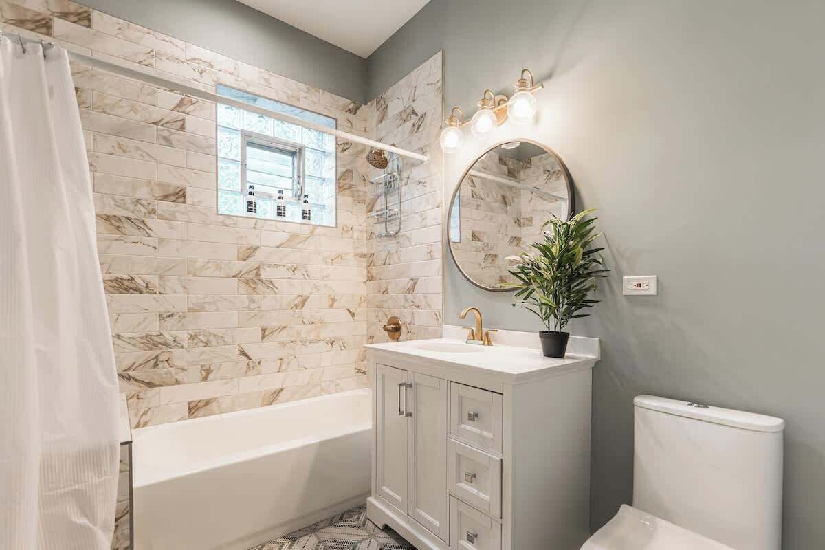 A bathroom with a marble backsplash, a bathtub, a sink with a mirror, and a potted plant.