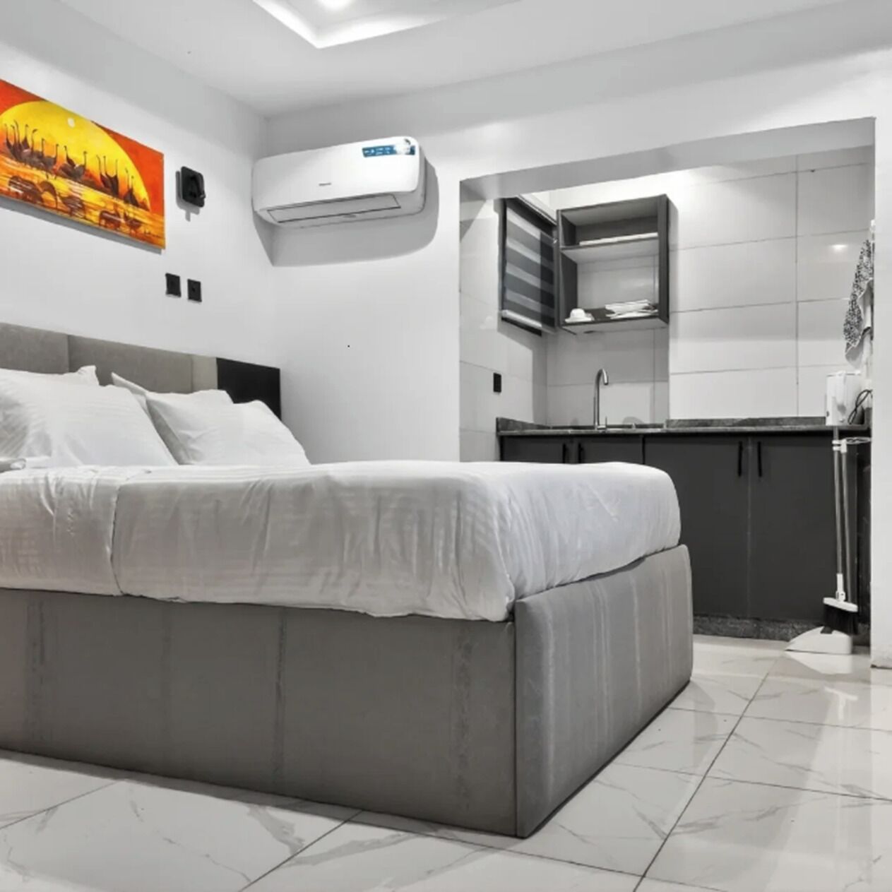 Ein modernes Schlafzimmer mit einem großen Bett, einer kleinen Küchenzeile und einer Klimaanlage.