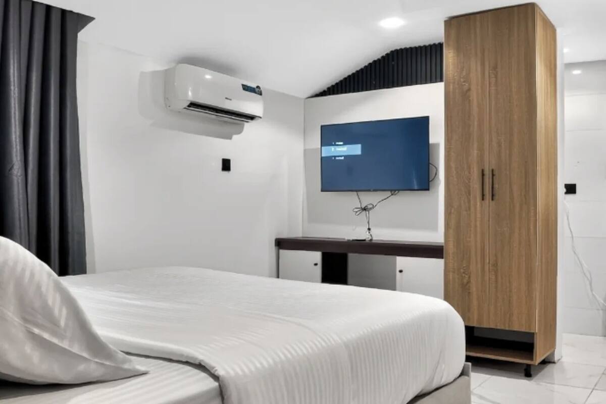 A bedroom with a bed, a TV mounted on the wall, and a wardrobe.