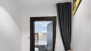 Un soggiorno moderno con due divani beige, una tenda scura e vista su una zona cucina.
