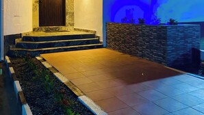 Ingresso moderno di una casa con porta in legno, scalini che conducono ad essa e un muro in pietra con elemento decorativo d'acqua.