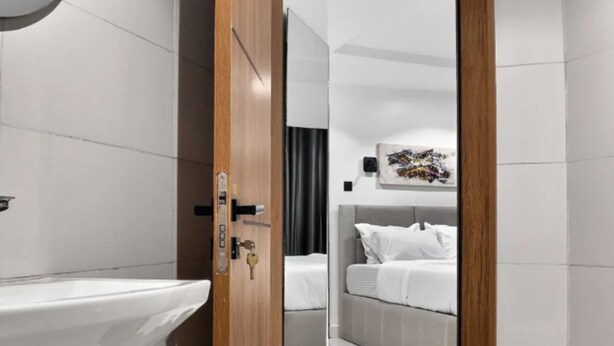 Un bagno moderno con una porta in legno, un lavandino bianco e uno specchio a parete.