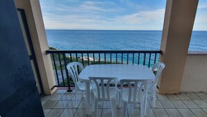 Ein Balkon mit weißem Tisch und Stühlen, der Blick auf die Küste freigibt.