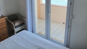 Ein Schlafzimmer mit Bett, Stuhl, Schreibtisch und Blick auf den Strand durch eine Schiebetür.