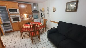 Ein kompakter Wohnbereich mit Esstisch, Stühlen, einer schwarzen Couch und einer Küchenzeile mit Mikrowelle, Backofen und Kaffeemaschine.