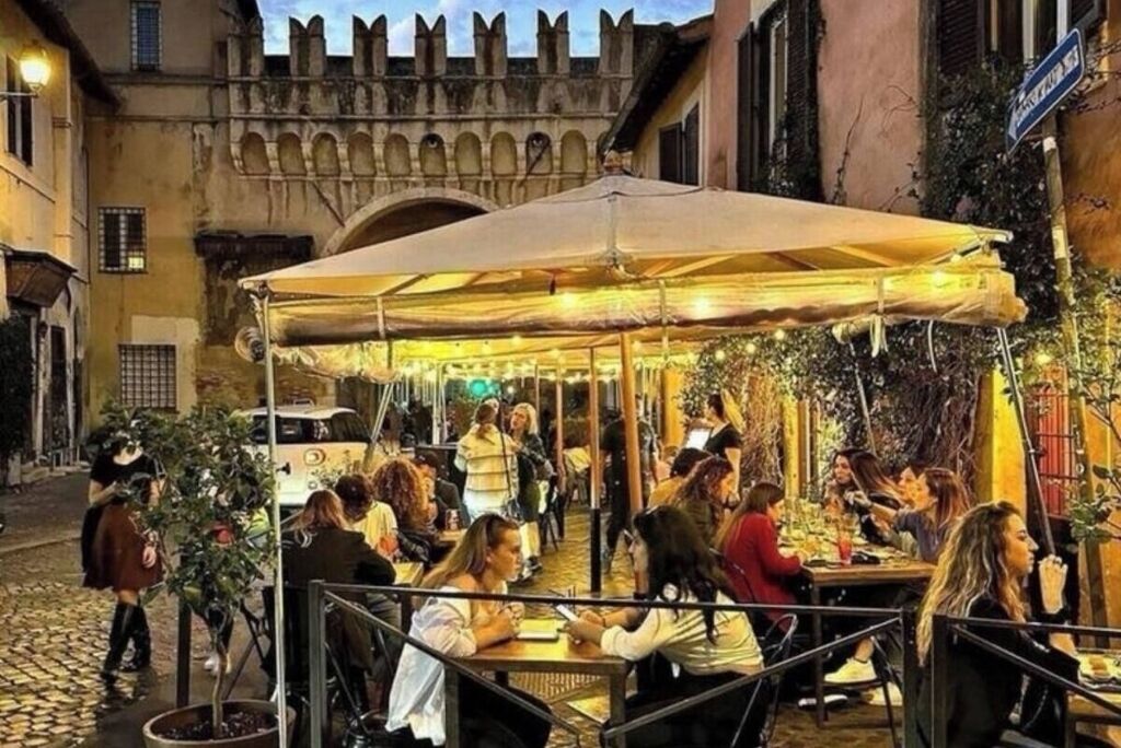 Ein Straßencafé mit Tischen und Stühlen, umgeben von Kopfsteinpflaster und historischen Gebäuden.