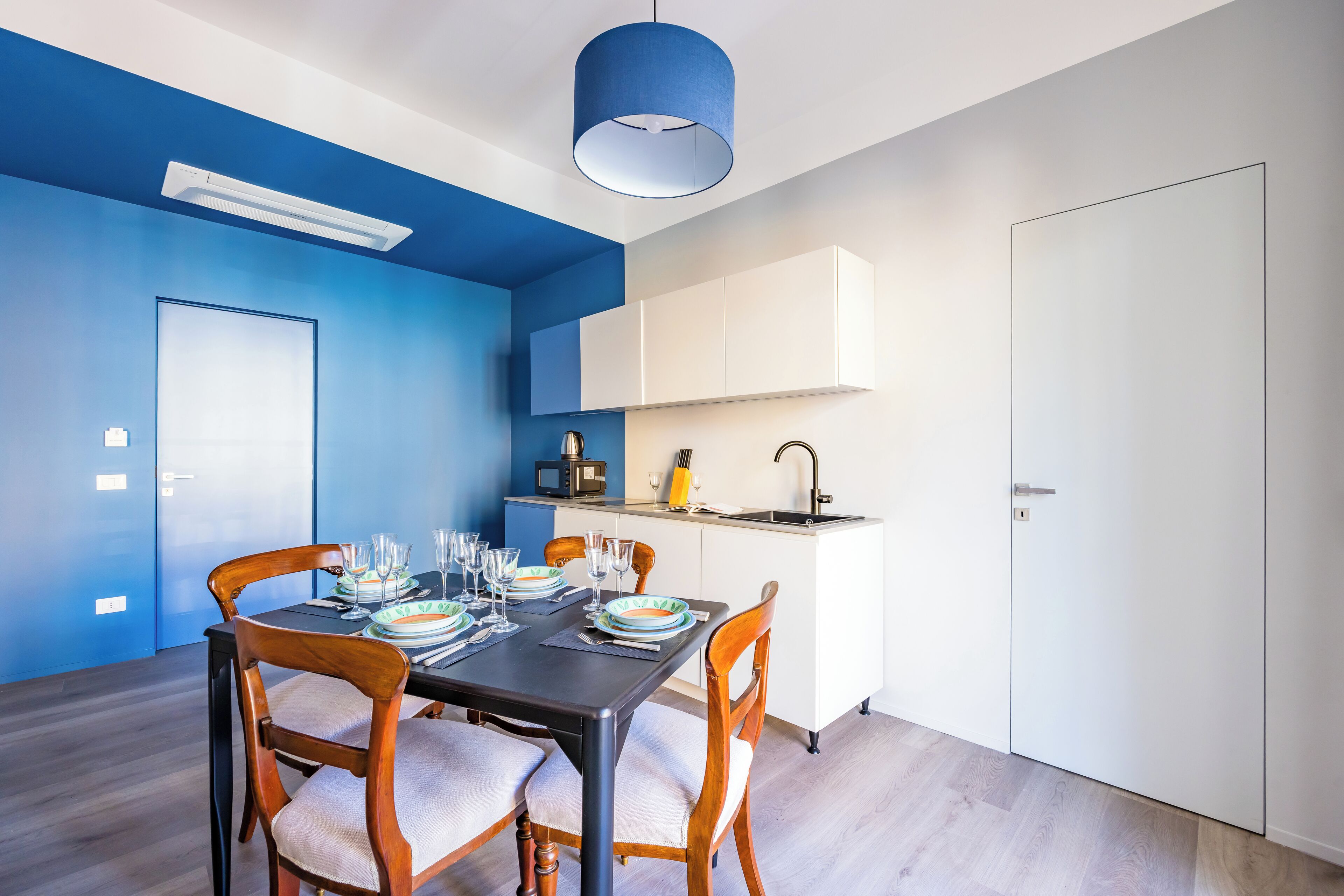 A modern dining area with a blue accent wall, white cabinetry, and a compact kitchen area.