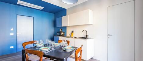 A modern dining area with a blue accent wall, white cabinetry, and a compact kitchen area.