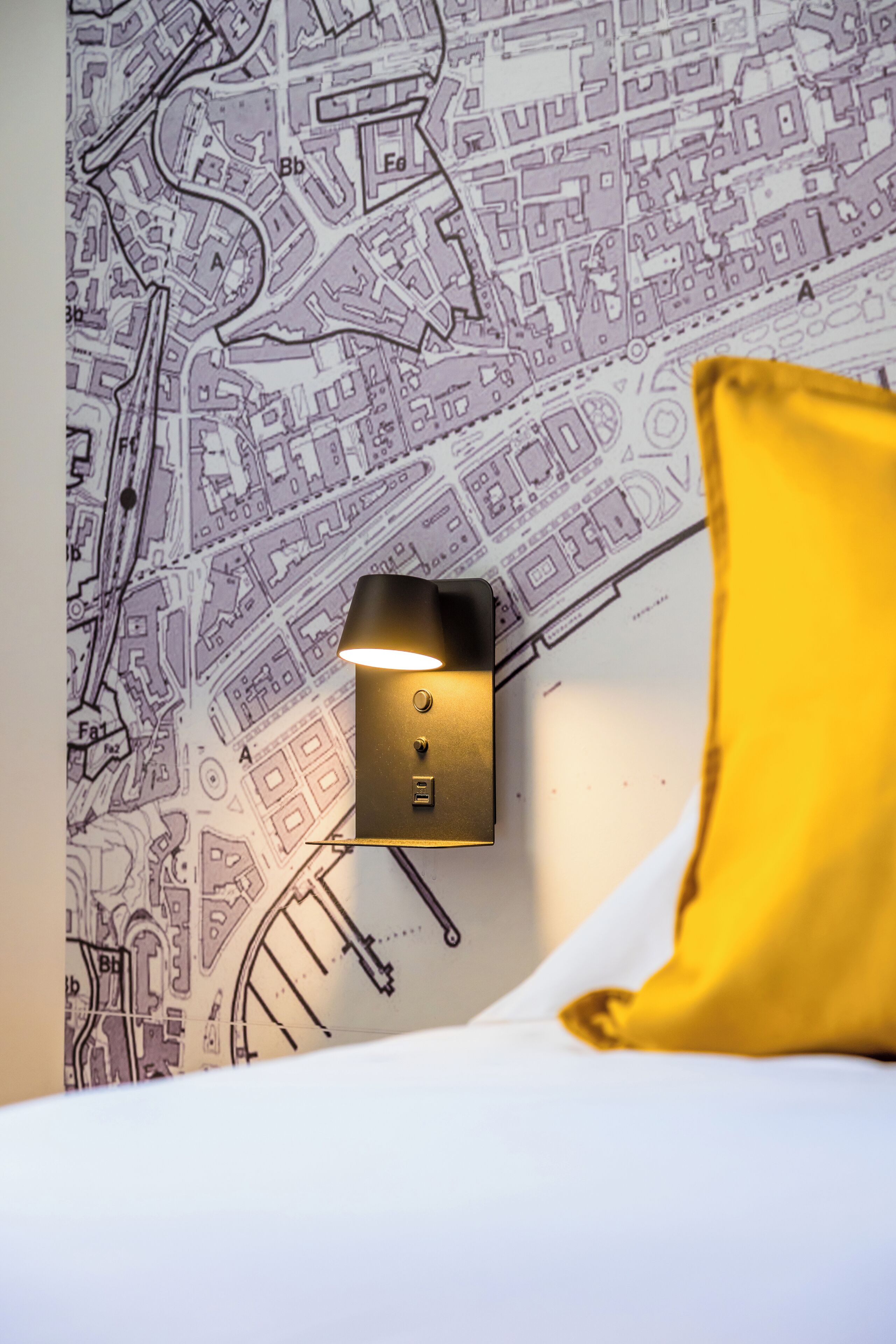 A bed with a yellow pillow, a wall map, and a wall-mounted light fixture.