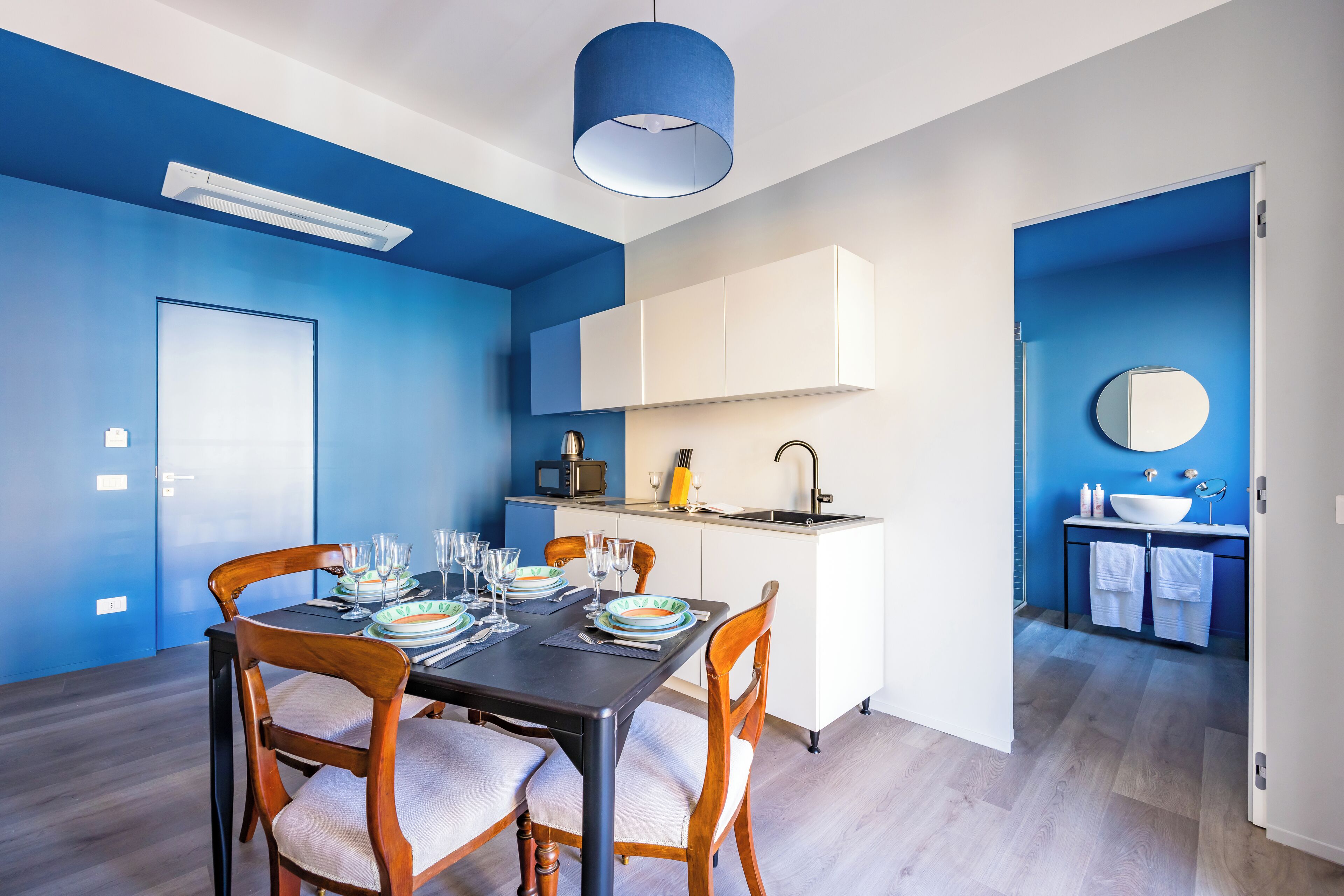 A modern kitchen with white cabinets, a blue ceiling, and a dining area with wooden chairs and a table set for four.