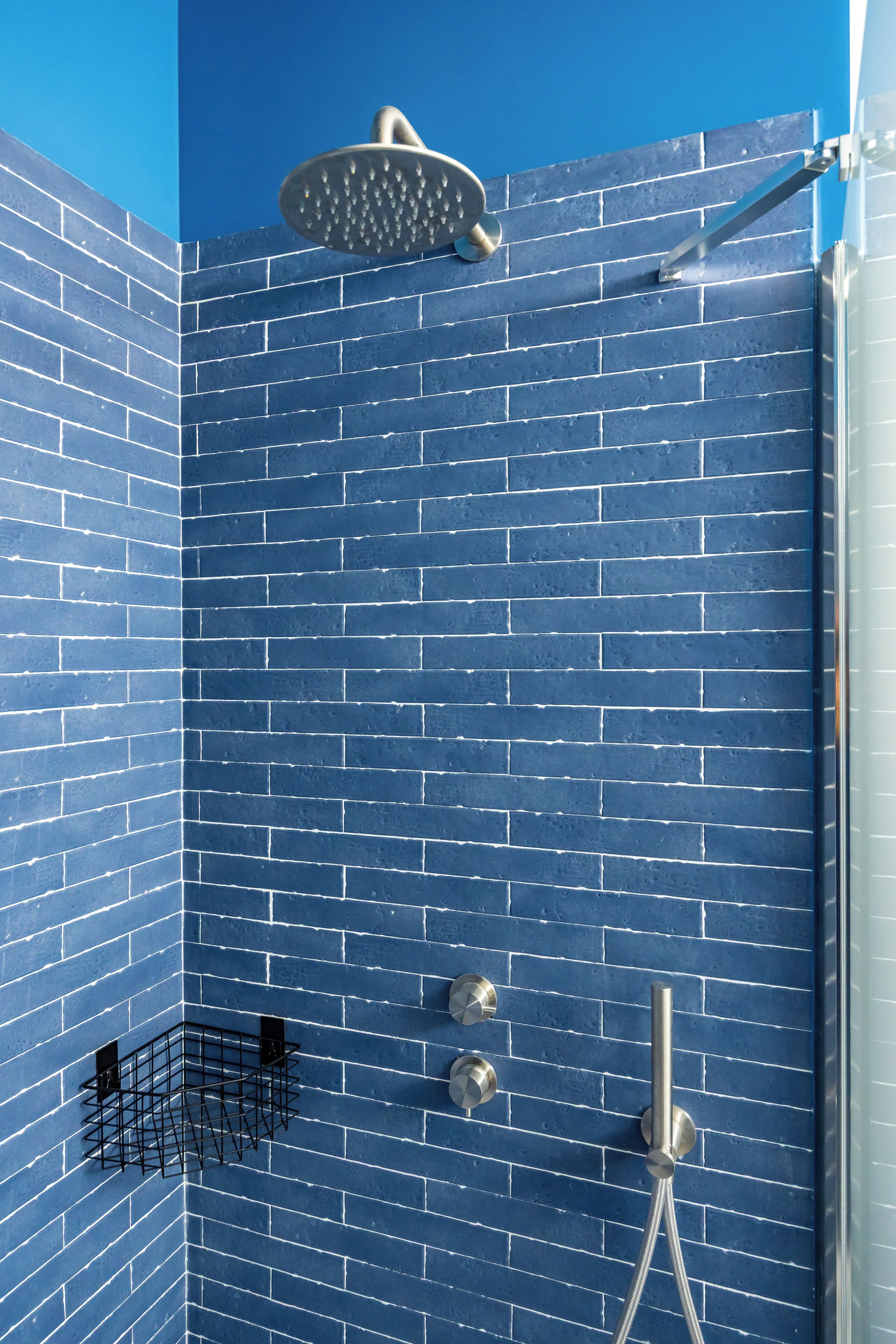 Une douche avec un mur recouvert de carreaux bleus, un pommeau de douche à main et un robinet fixé au mur.