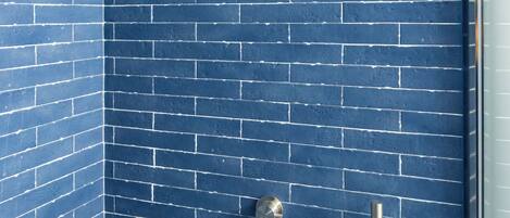 A shower with a blue-tiled wall, a handheld showerhead, and a wall-mounted faucet.