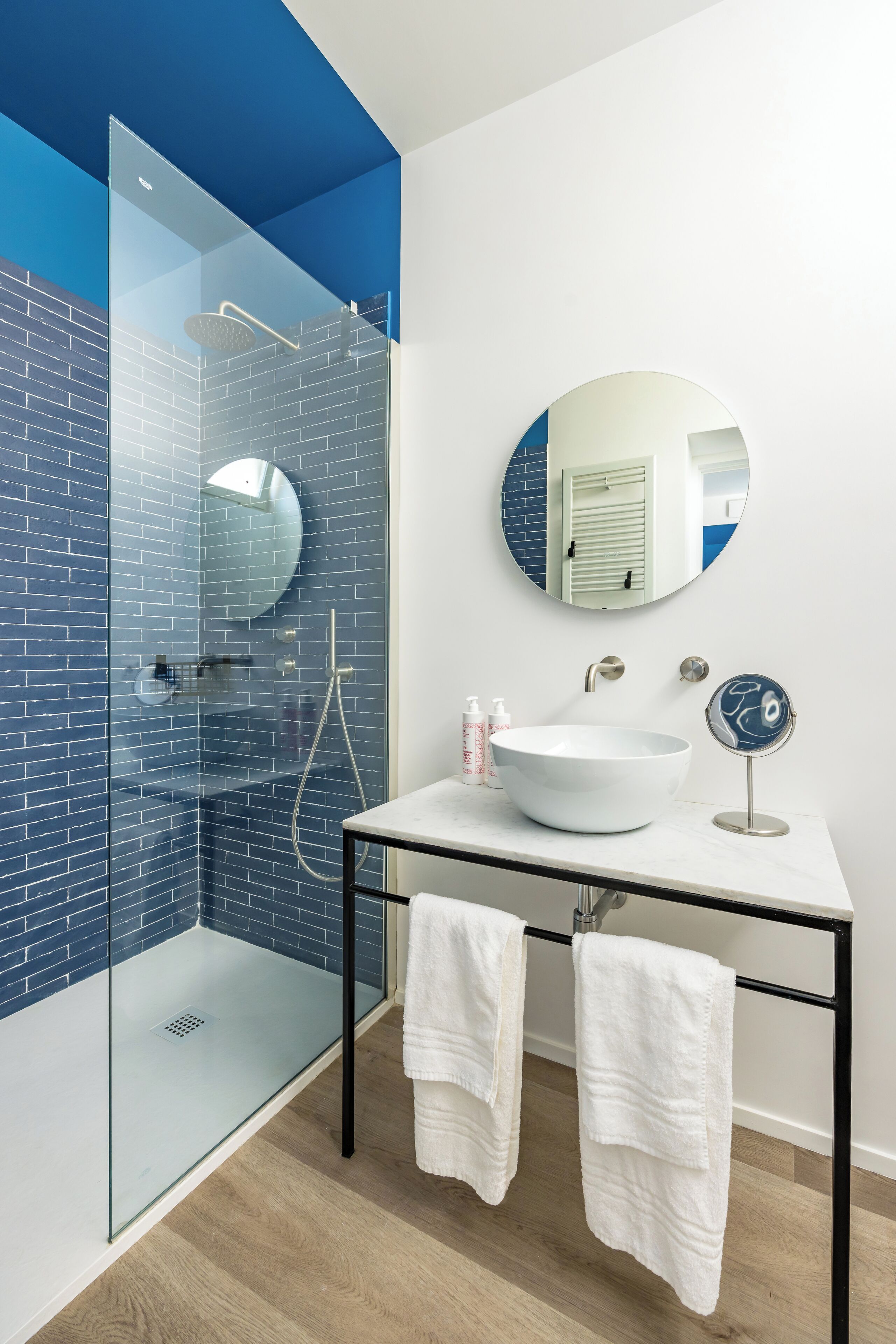Een moderne badkamer met een douchecabine van glas, een wit wastafelmeubel en een ronde spiegel.