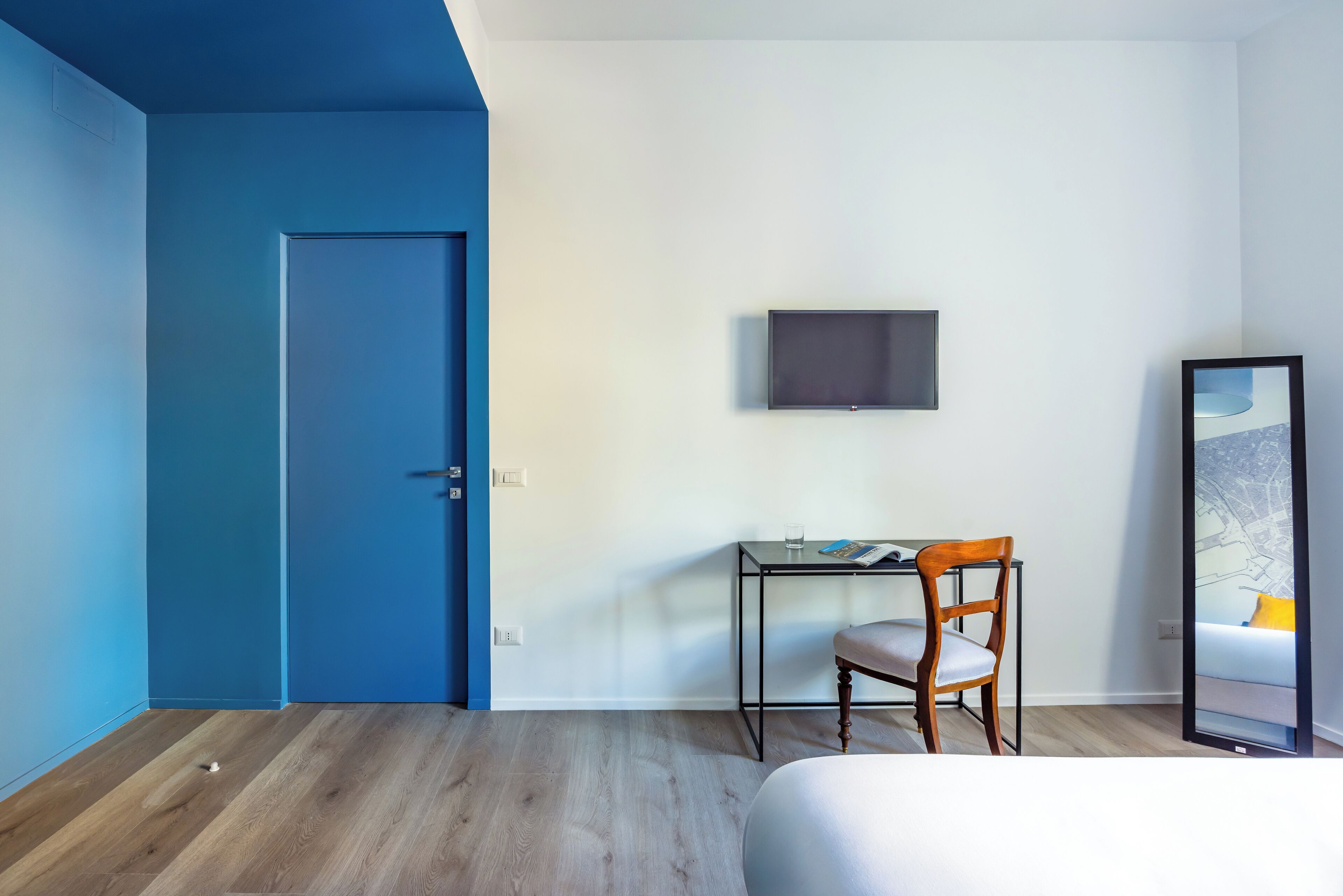 A bedroom with a bed, a desk with a chair, a television, and a door.