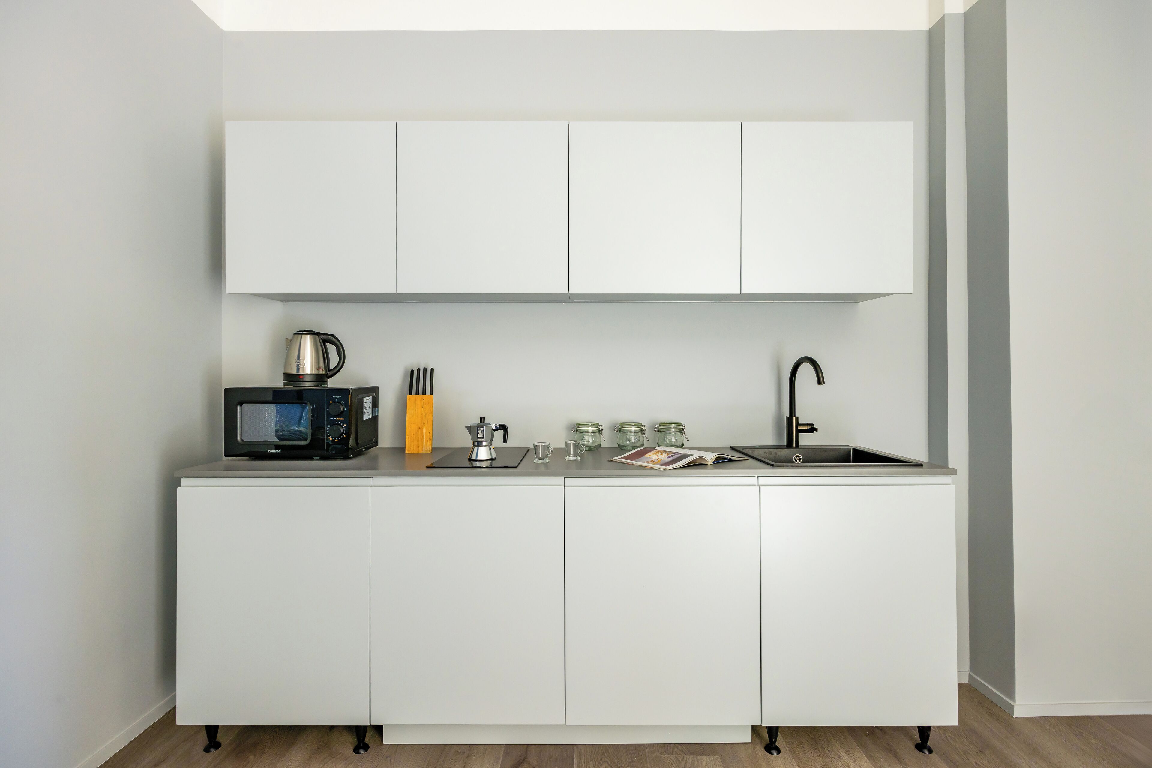 A compact kitchenette with a microwave, kettle, coffee maker, and a sink.