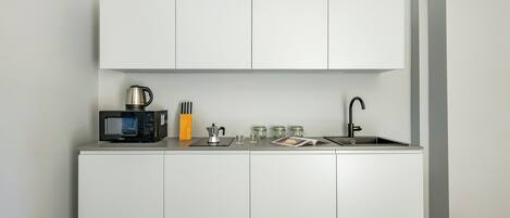 A compact kitchenette with a microwave, kettle, coffee maker, and a sink.