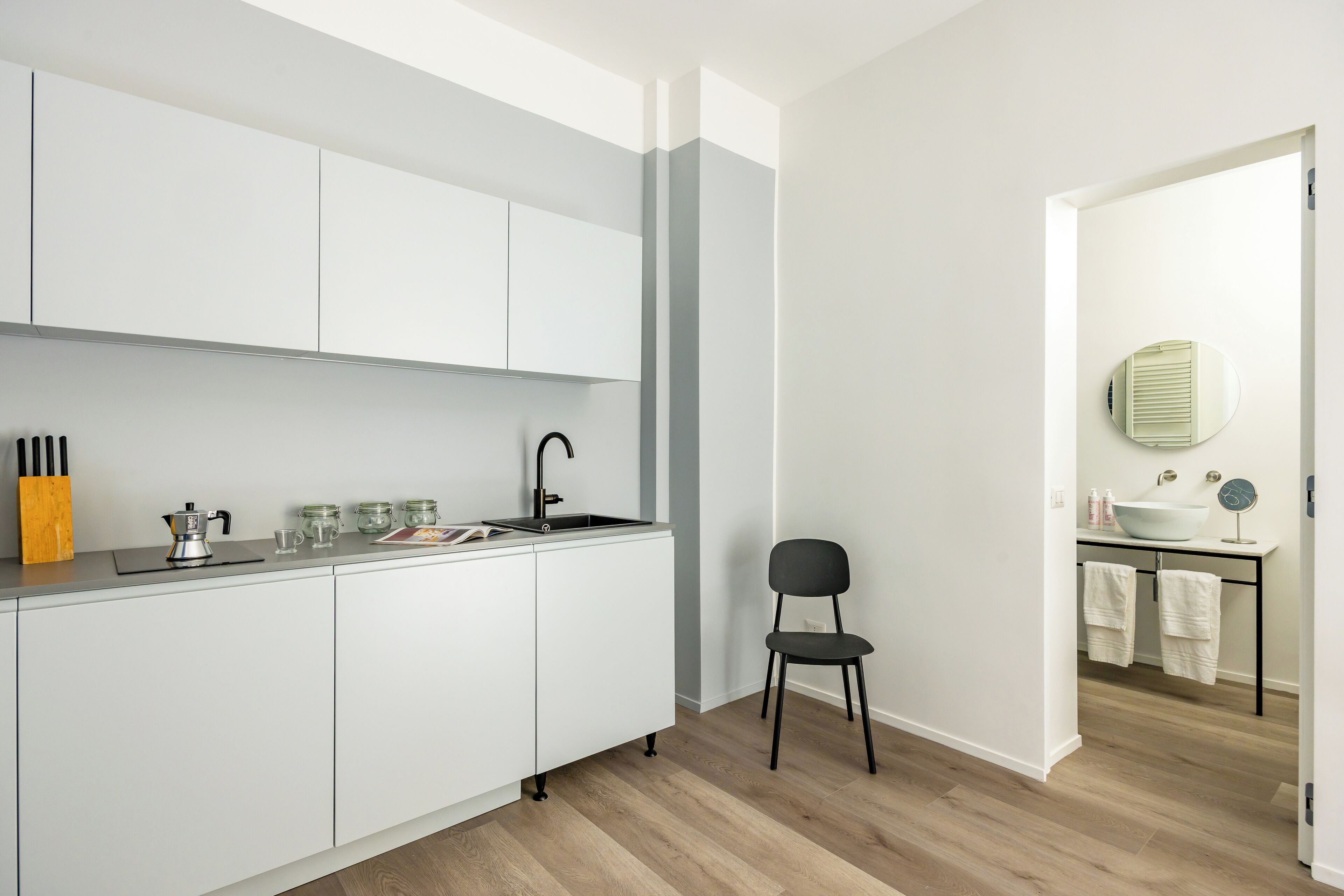 A modern kitchen with white cabinets, a black chair, and a wooden floor.