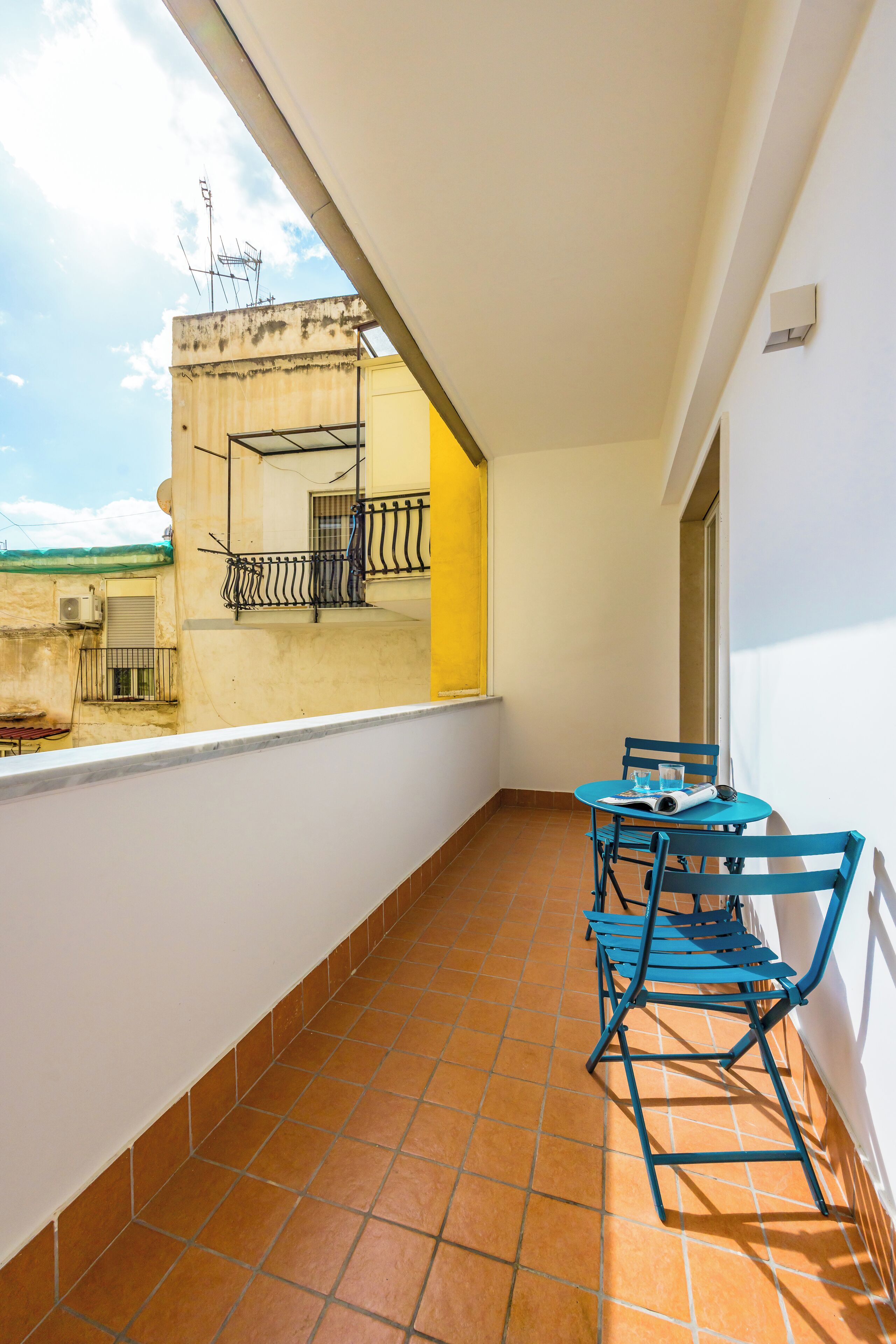 Ein Balkon mit Fliesenboden, einem Tisch mit Stühlen und einem Fenster mit Blick auf ein Gebäude.