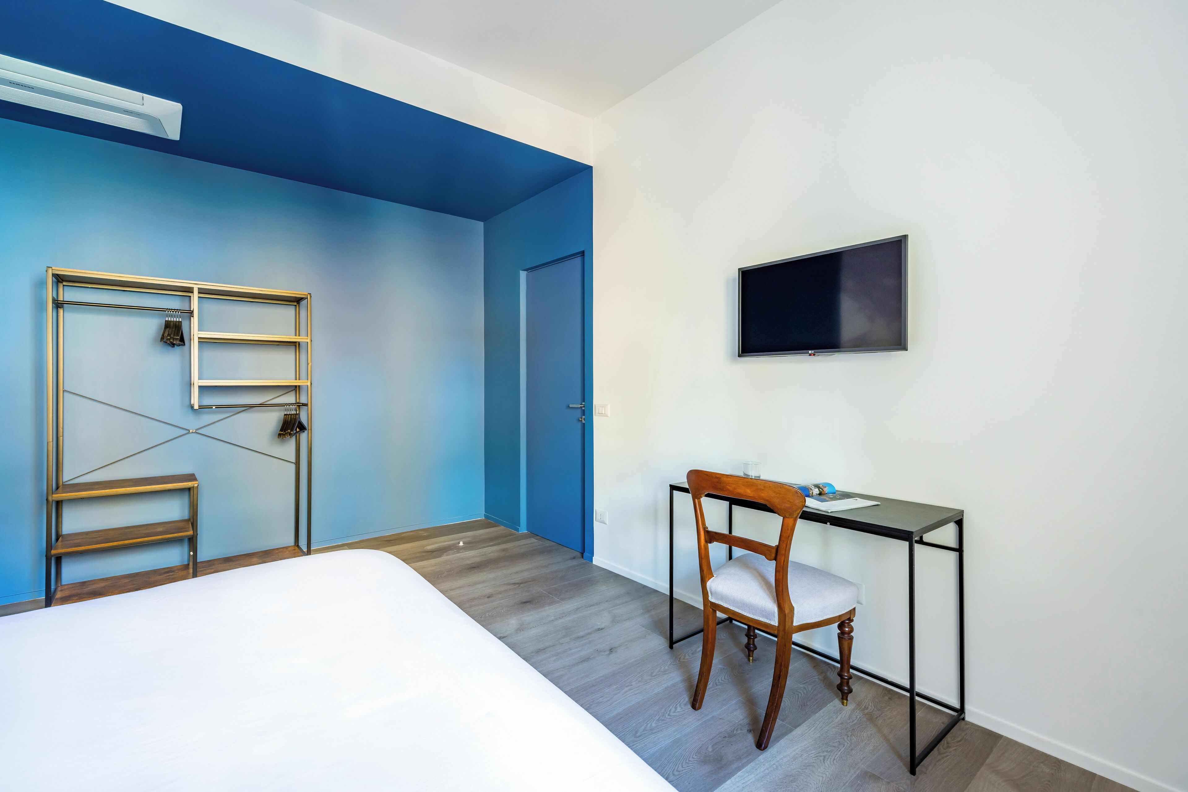 Quarto com cama, escrivaninha com cadeira, televisão e armário com escada.