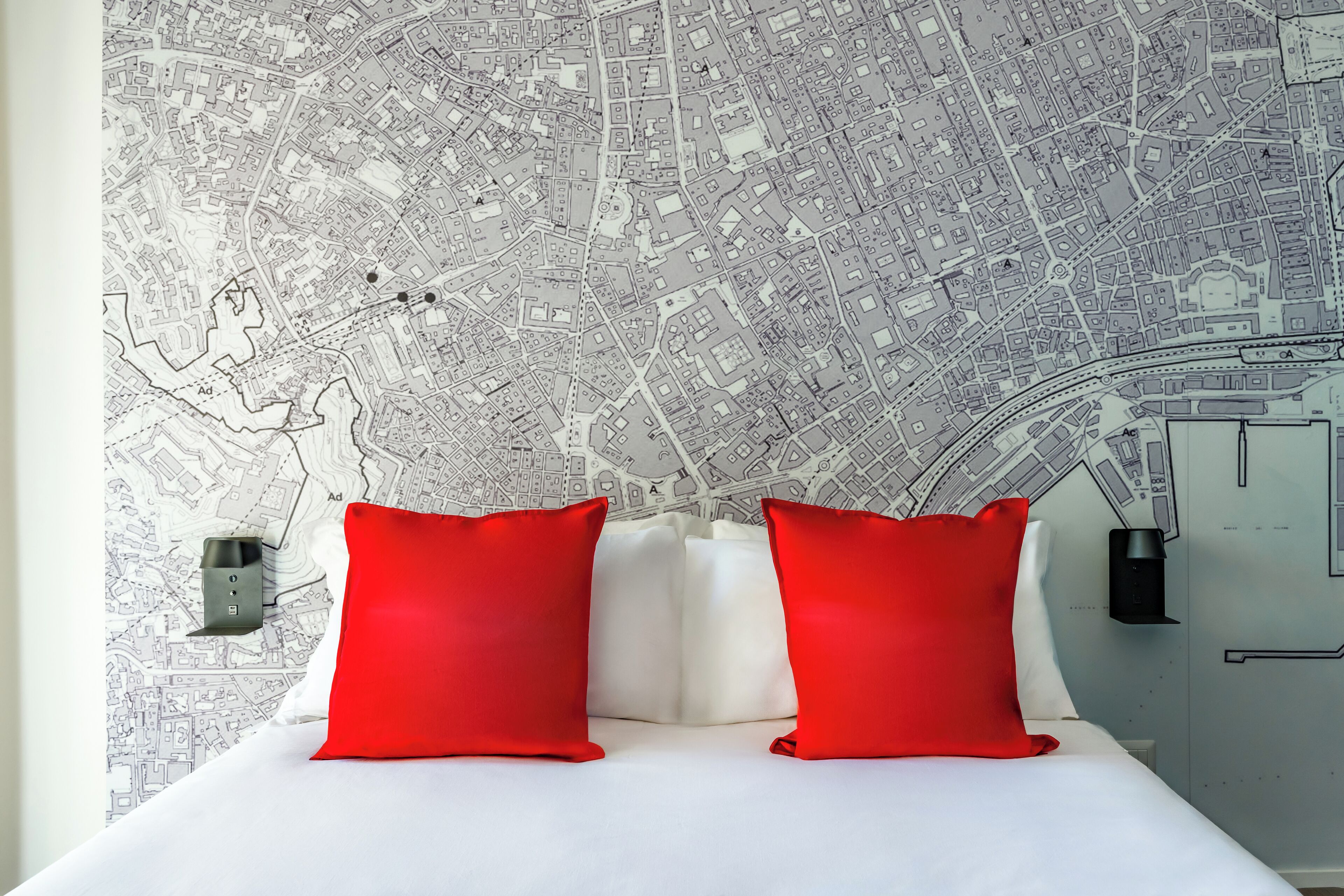 A hotel room with a large bed, two red pillows, a white headboard, and a wall map.