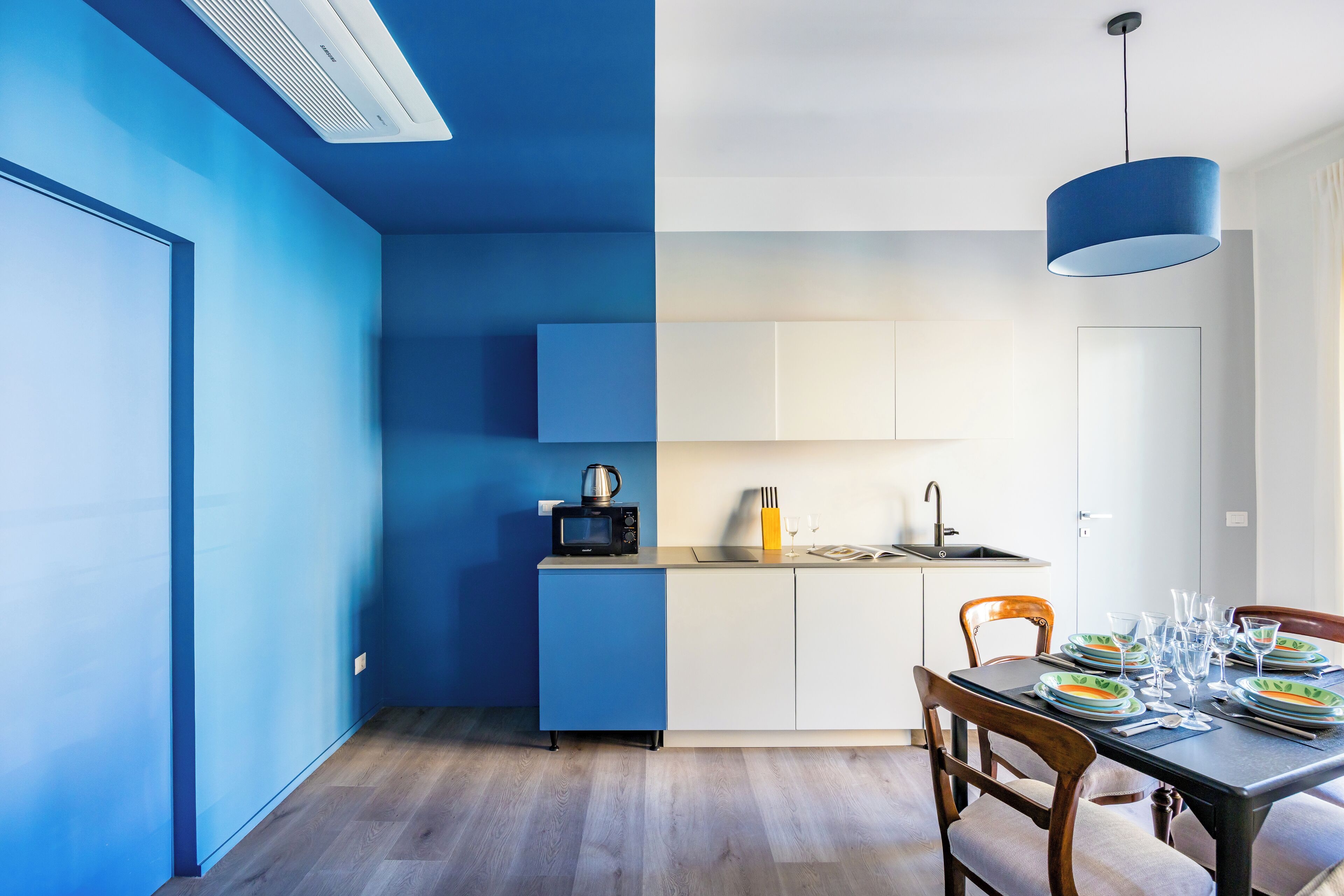 A modern kitchen with blue and white cabinetry, a microwave, and a dining area with a table set for four.