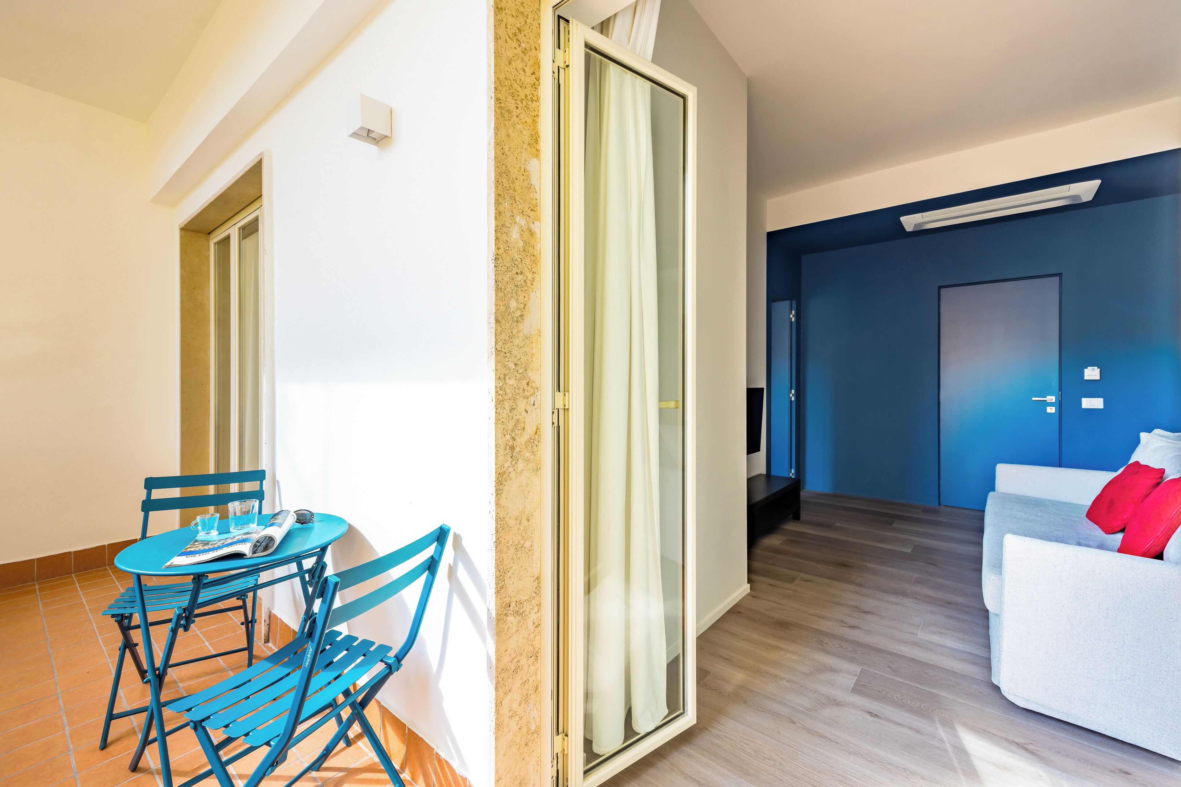 Un salón moderno con un sofá blanco, un sillón azul y una pequeña mesa con una revista.