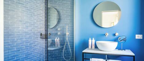 A bathroom with a glass-enclosed shower, a round mirror, a white sink, and a blue-tiled wall.