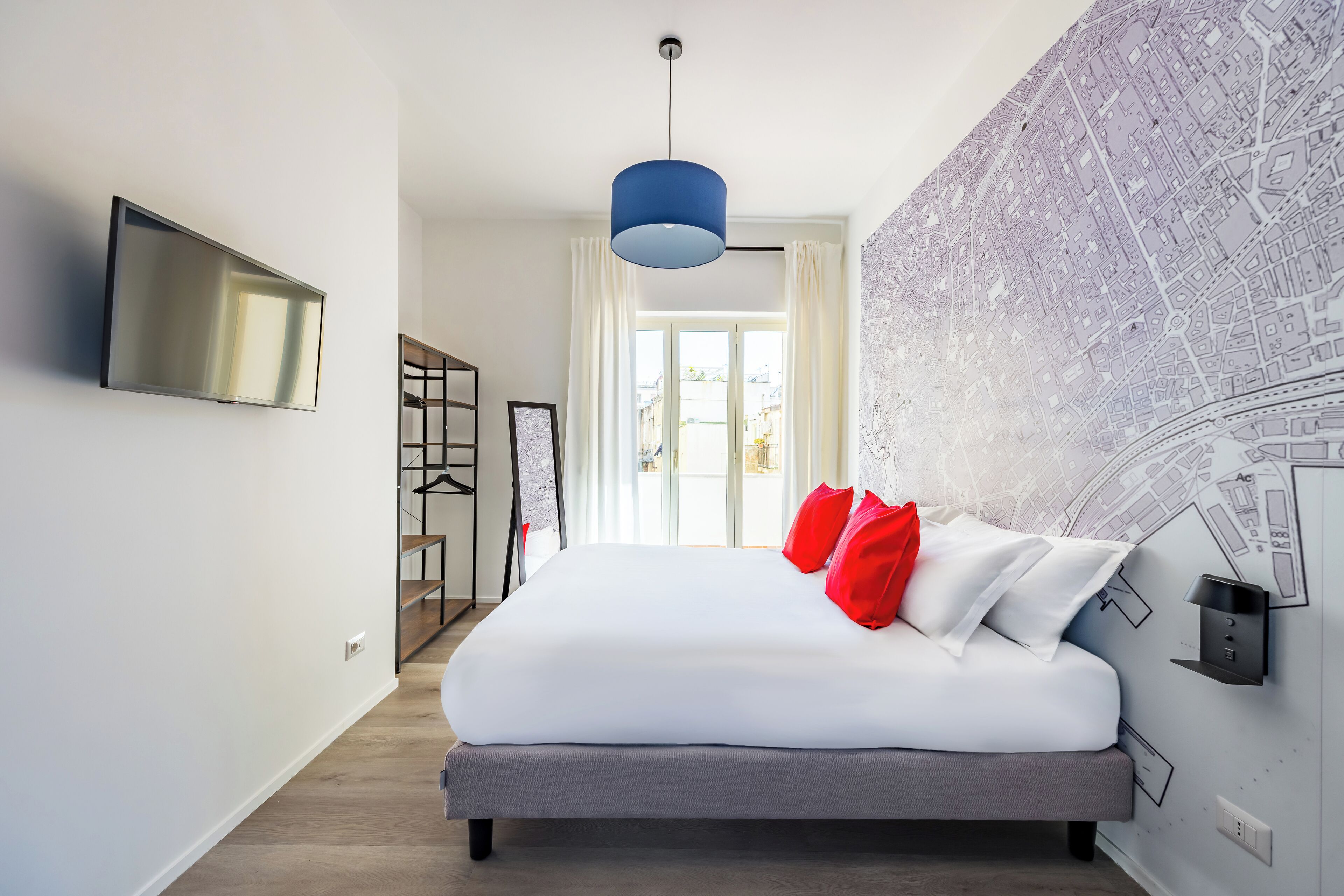 Ein modernes Hotelzimmer mit einem großen Bett, einem Flachbildfernseher, einer Wandmalerei mit einer Karte und einer blauen Pendelleuchte.