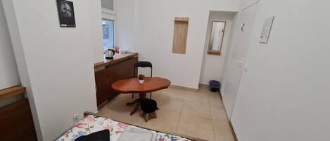 Une petite pièce, de taille modeste, comprenant un lit, un bureau et une chaise. Une fenêtre laisse entrer la lumière naturelle, et une petite table est accompagnée d’une chaise.