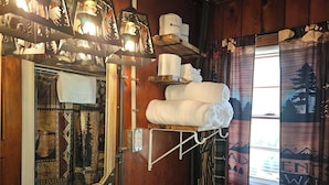 A rustic bathroom with wooden walls, a mirror, a towel rack, and a window with a view of mountains. - The Huntsmen (Hillsboro)