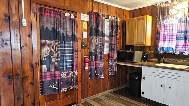 A wooden interior with a kitchen area, including a microwave, sink, and cabinets. - The Huntsmen (Hillsboro)