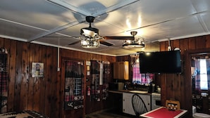 A cozy room with wooden walls, a ceiling fan, a TV, a small kitchenette, and a dining area with a table and chair. - The Huntsmen (Hillsboro)