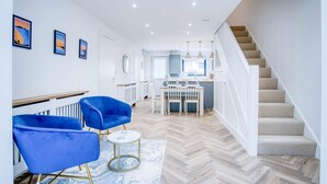 A modern interior with a staircase, a dining area with blue chairs, and a kitchen. - Hatherleigh Drive - 2 Bedroom House - Mumbles (Swansea)
