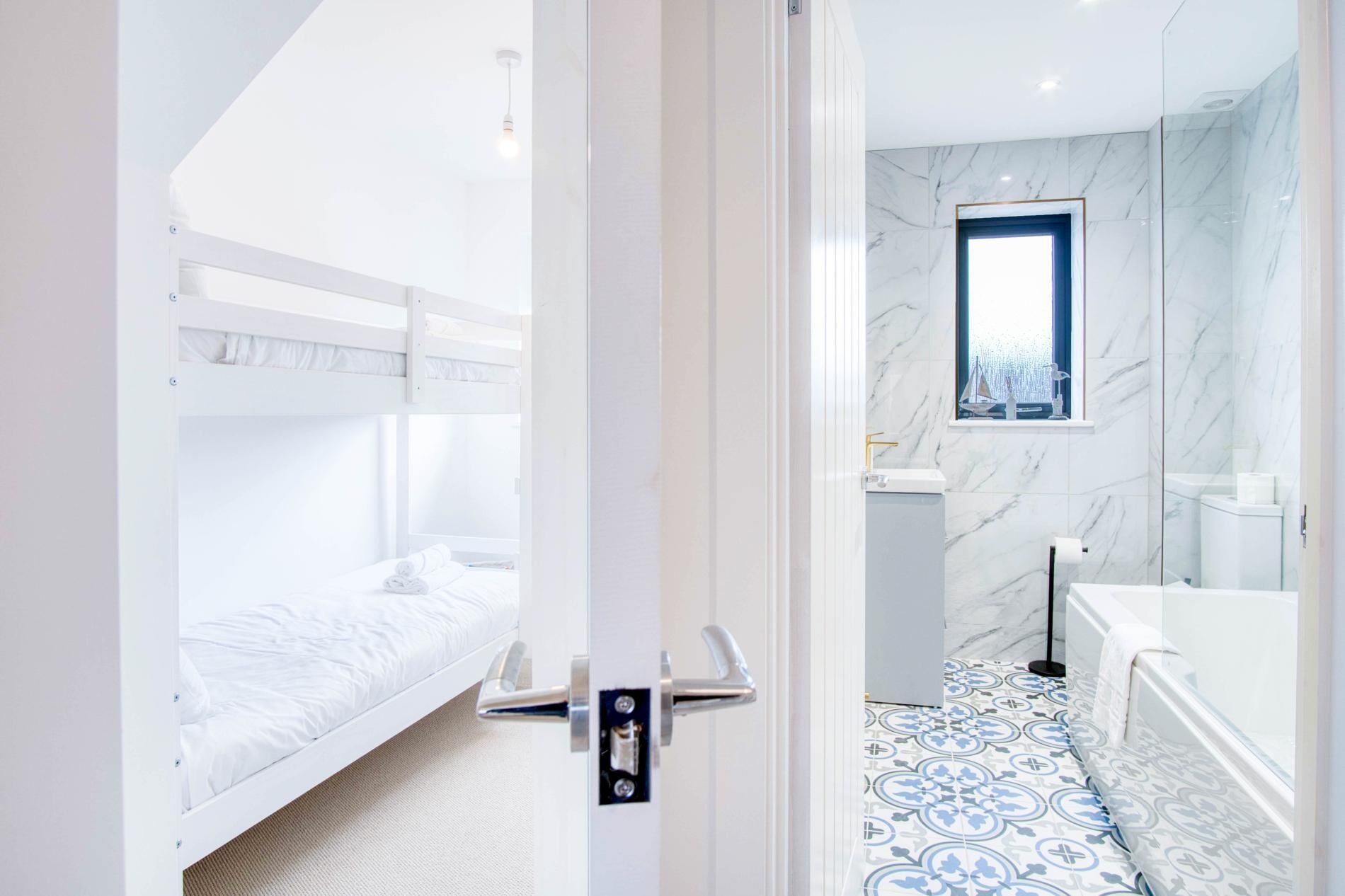 Een moderne hotelkamer met een stapelbed, een badkamer met een marmeren douche en een kamer met een vloerbedekking met een patroon.