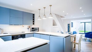 A modern kitchen with blue cabinets, a central island, and pendant lighting. - Hatherleigh Drive - 2 Bedroom House - Mumbles (Swansea)