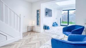 A modern interior with a herringbone floor, a blue armchair, a small table, and a wall-mounted TV. - Hatherleigh Drive - 2 Bedroom House - Mumbles (Swansea)