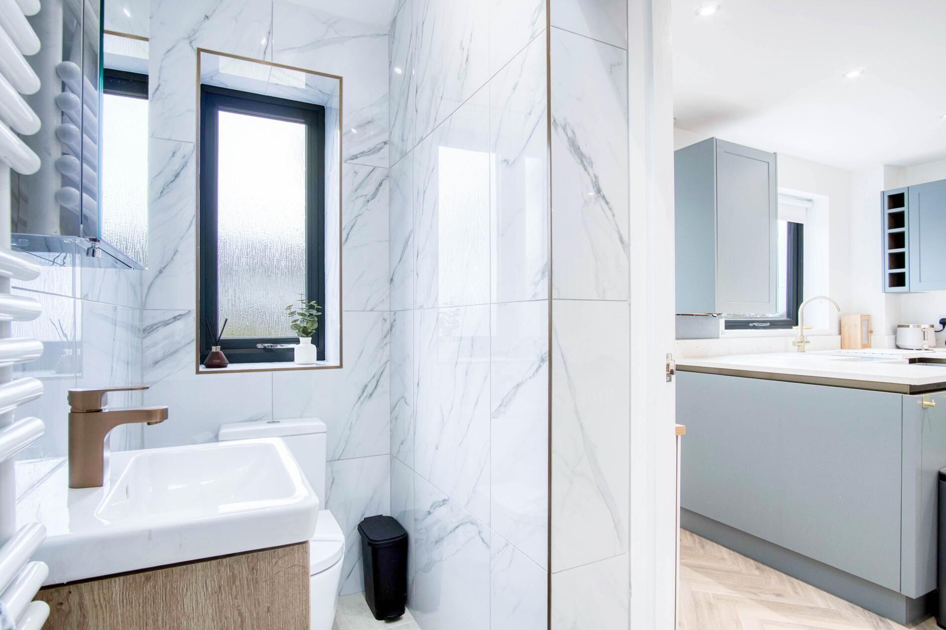 Een moderne badkamer met een grote spiegel, witte marmeren tegels, een wastafel en een toilet.