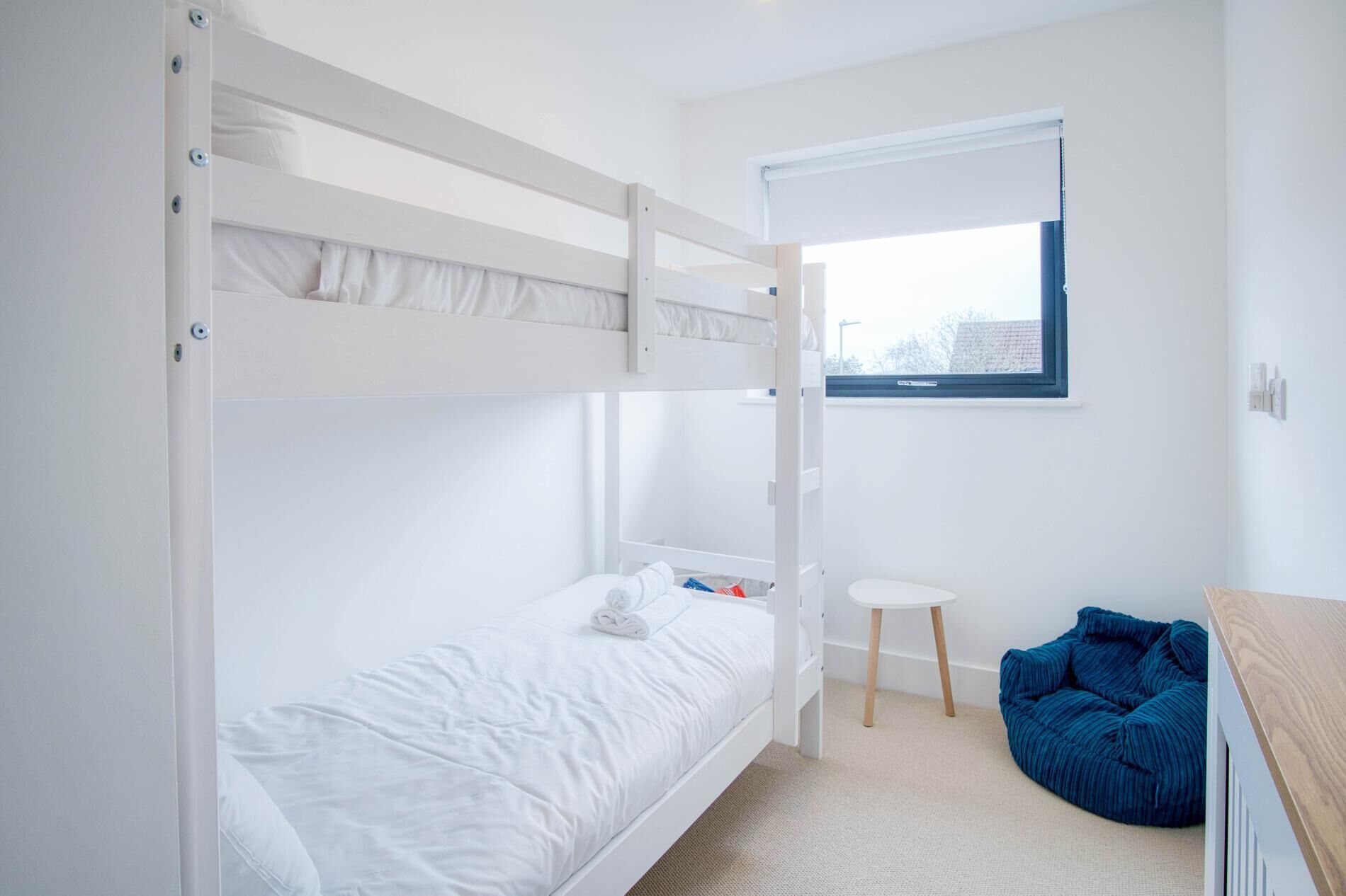 A bunk bed room with a small table and a blue bean bag chair.