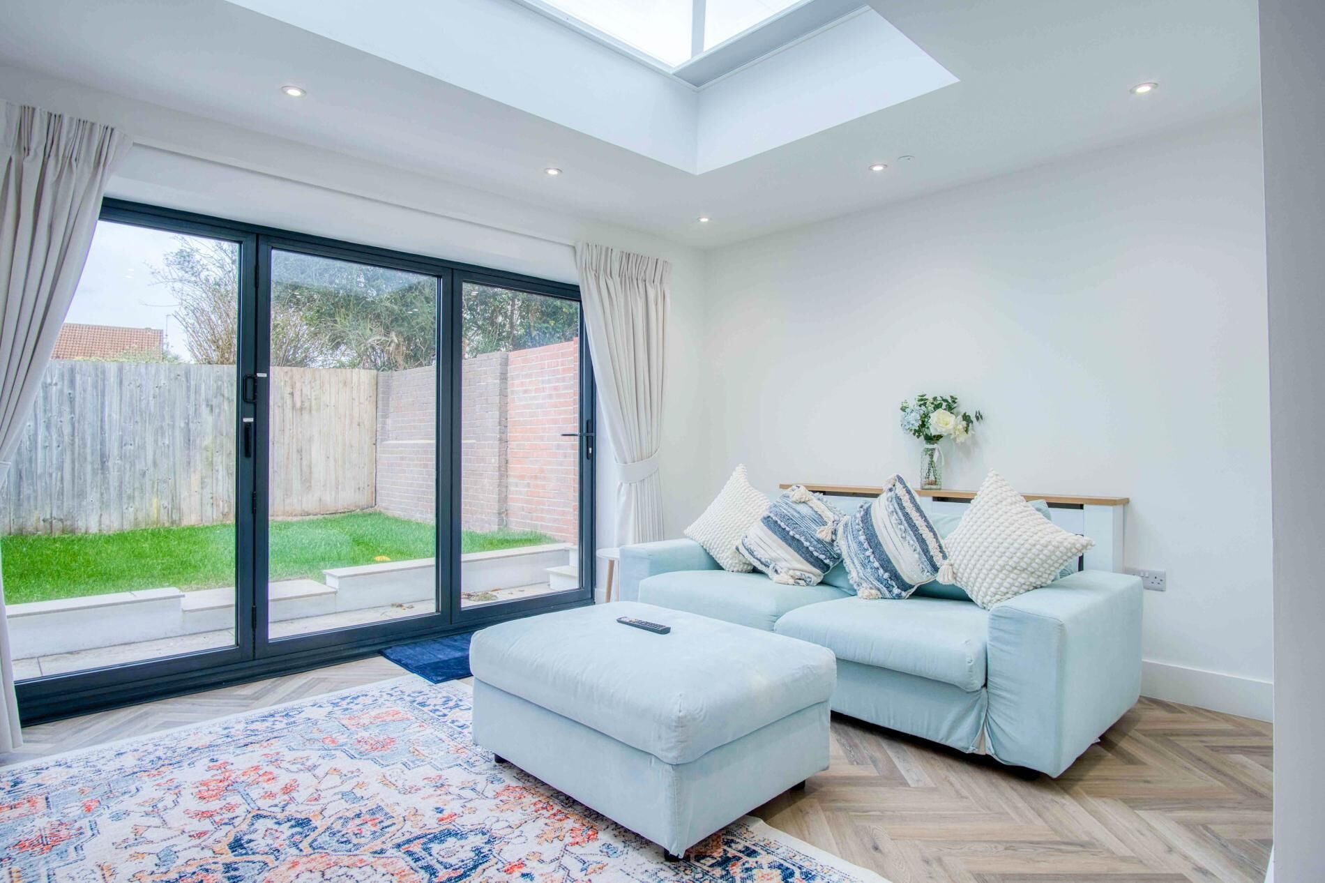 A spacious living room with a light blue sofa, a matching ottoman, and a large sliding glass door leading to a backyard.