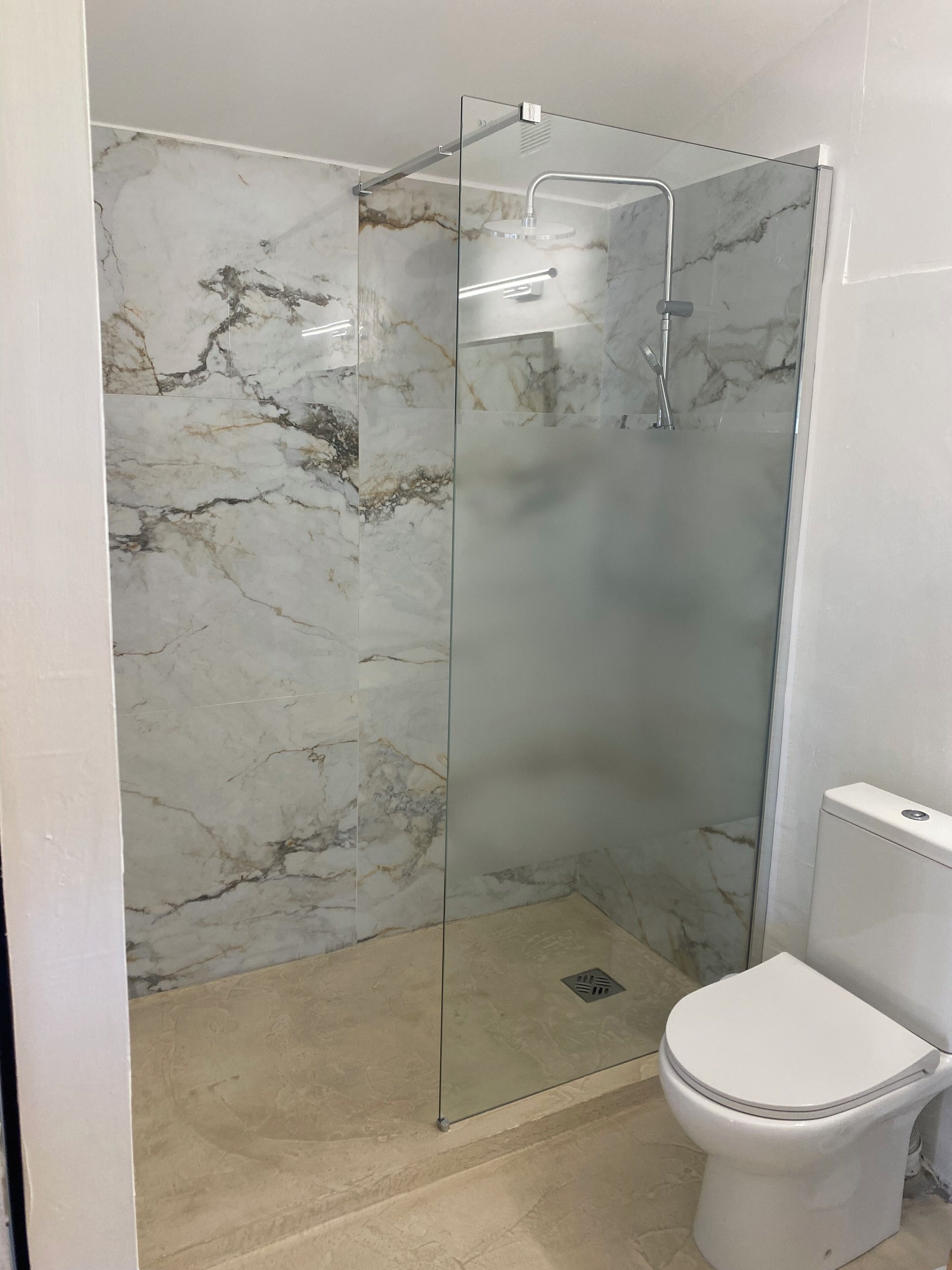 A bathroom with a glass-enclosed shower, a white toilet, and marble-patterned walls.