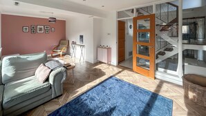 A living room with a sofa, a chair, a blue rug, a wooden door, and a staircase. - 4 bedroom accommodation in Sarisbury Green, Southampton (Sarisbury Green, Southampton)