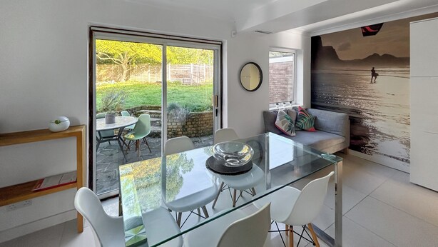 A modern kitchen with a glass dining table, white chairs, a built-in oven, and a large window with a view of a garden. - 4 bedroom accommodation in Sarisbury Green, Southampton (Sarisbury Green, Southampton)