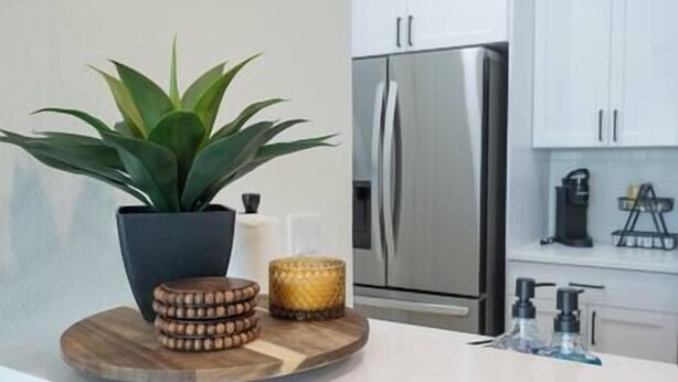 A modern kitchen with a stainless steel refrigerator, a potted plant, and a wooden serving tray with coasters and a candle. - Brick City Lofts Downtown Ocala Unit 303 (Ocala)