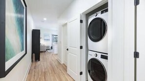 A laundry room with two stacked washing machines and a door leading to another room. - Brick City Lofts Downtown Ocala Unit 303 (Ocala)
