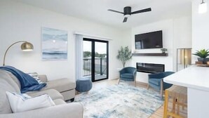 A modern living room with a sofa, a coffee table, a TV mounted on the wall, and a balcony with a view. - Brick City Lofts Downtown Ocala Unit 303 (Ocala)